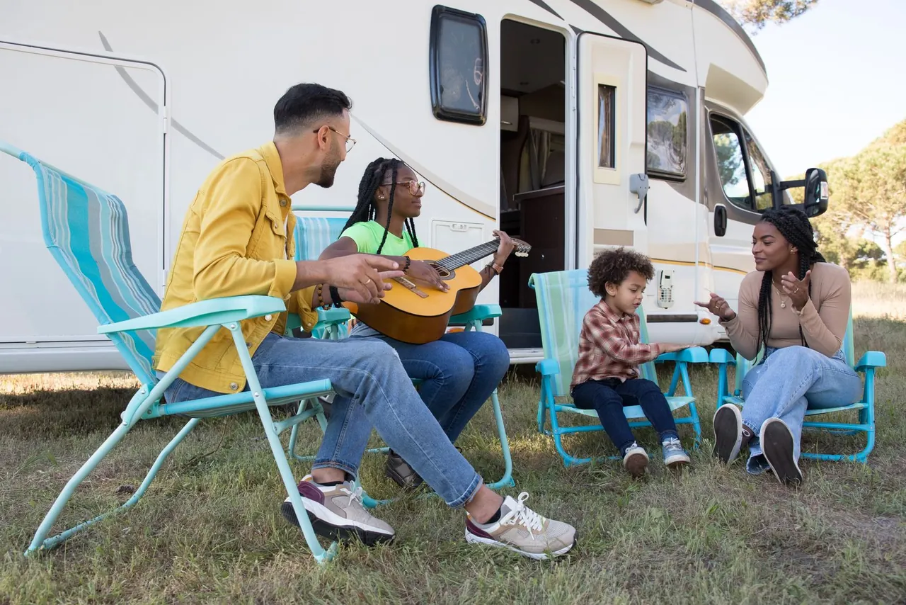 A family relaxing in camping chairs beside their touring caravan
